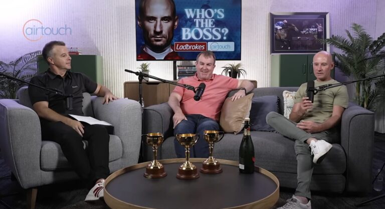 Branded podcast production session in The Brickworks studio at The Plot Studios North Sydney — three guests recording with professional microphones, branded screen backdrop and racing trophies on the coffee table
